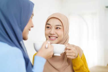 Mutlu Asyalı Müslüman kadınlar oturma odasında çay ya da kahve içip iş konuşuyorlar. Modern Müslümanlar yaşam tarzı konsepti.