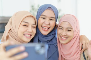 Mutlu Asyalı Müslüman kadınlar selfie çekiyorlar ya da akıllı telefon kullanarak sosyal ağda canlı yayın yapıyorlar..