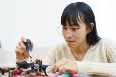 Mutlu Asyalı etnik kökenli kadın üniversite öğrencisi robotik ve programlamayı kendi başına öğreniyor, kadın bir robot ve kodlama yapıyor.