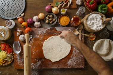 Neşeli İtalyan şef mutfaktaki ahşap masada taze pizza hamuru yapıyor..