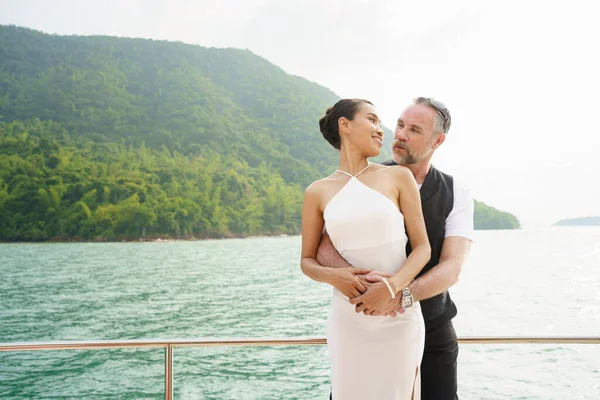 Happy Asian and caucasian white couple celebrating their marriage anniversary together on the yacht. Adult couple sailing a yacht and drinking a Champaign together during a honeymoon trip.