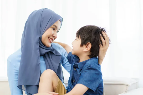 Happy cheerful Asian muslim family living together in a weekend, woman muslim embracing her lovely little son and smiling to camera. Modern muslim lifestyles concept.
