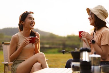 Mutlu Asyalı genç kadınlar. Göl ormanında kamp yapan ve çay ya da kahve içen arkadaşlar. Yazın doğa parkında kamp yapan bayan arkadaşlar..