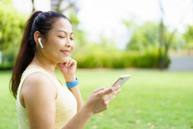 Sağlıklı mutlu Asyalı kadın parkta koşmaktan ve koşarken kablosuz kulaklıkla müzik dinlemekten hoşlanır. Güzel Asyalı kadın koşarken kulaklıkla müzik dinliyor..
