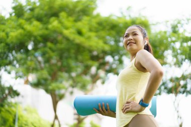 Mutlu güzel Asyalı kadın yoga ve arabuluculuk egzersizi hazırlamak için çim tarlasında yoga minderi seriyor. Kadın yoga ya da vücut ağırlığı ve meditasyon egzersizi hazırlıyor..