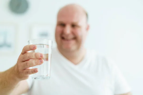 Happy cheerful oversize large belly man wake up in the morning and sitting on the bed then drinking a water in a glass. Caucasian white fat man drinks a water in a drinking glass in every morning.