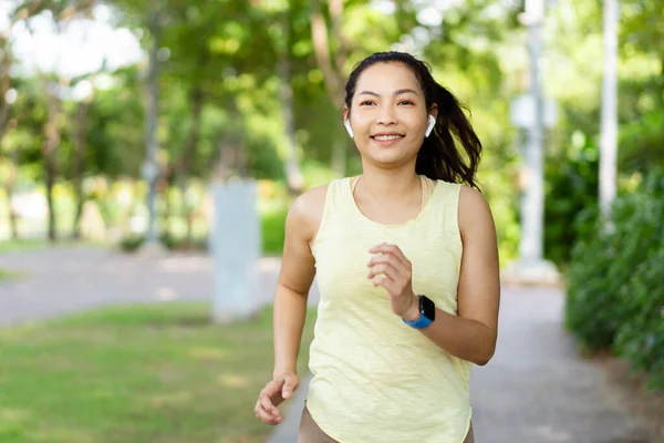 Healthy happy Asian woman enjoy running exercise at the park and listening music on wireless headphone while running. Beautiful Asian woman listening music on an earphones while running.