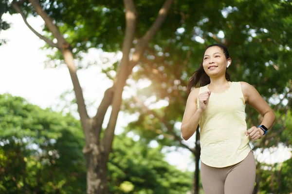 Healthy happy Asian woman enjoy running exercise at the park and listening music on wireless headphone while running. Beautiful Asian woman listening music on an earphones while running.
