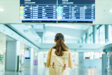 Mutlu Asyalı güzel bayan sırt çantalı turist havaalanı terminalinden kalkış ve varış bilgilerine bakıyor, yalnız kadın turist konsepti. Uçuş programını kontrol eden kadın.