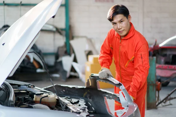 Professional Asian car technician repairing a broken car at the front bumper. Technician working repairing - fixing cars in garage.