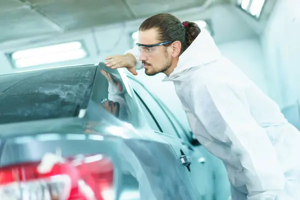 Professional automotive painting technician in chemical protecting suit inspecting car painting quality in painting chamber together. Car painting and detailing technicians portrait.