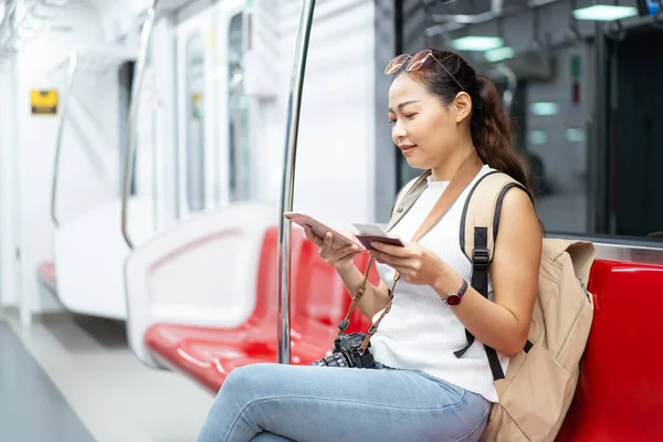 Güzel Asyalı kadın turist. Trende seyahat ederken akıllı telefonuyla şehir haritasını arayan yolcu. Kadın yolcu ulaşım bilgilerini aramak için cep telefonu kullanıyor.