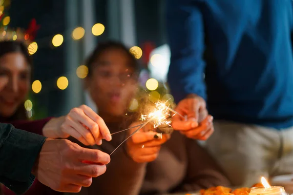 Group of diverse ethnicity young people enjoy celebrating a Christmas and New Year party together with a lot of foods and drinks and enjoy playing with sparkling bengal light - fireworks together.
