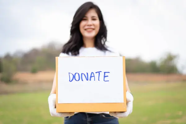 Happy Asian beautiful woman working as a volunteer holding a donation cardboard box portrait. Voluntary and charity works for humanity and sustainable concept. Female volunteer smiles to camera.
