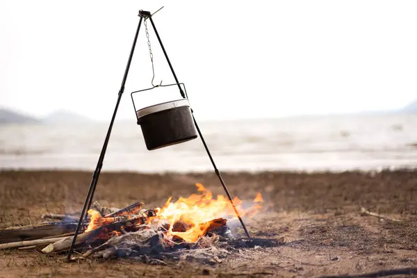 Boiling water in a small metal camping kettle - bowl on burning firewood. A small camping kettle on bonfire at the camping site. Outdoor activity concept.
