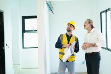 Beyaz erkek emlak müşterisinin portresi erkek inşaat ustabaşıyla inşaat ve iç işleri hakkında konuşuyor. İnşaat müteahhidi müşteriyle konuşuyor.