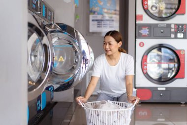 KIOSK mağazasında elinde kullanılmış kıyafet sepeti tutan mutlu Asyalı kadın. Çamaşır makinesinde çamaşır yıkayacak kadın KIOSK.