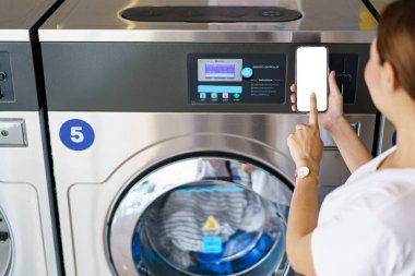 Mutlu Asyalı güzel kadın self servis çamaşır makinesi kullanıyor KIOSK ya da otomatik çamaşır makinesi satıcısı. Akıllı telefondan boş beyaz ekran gösteren bir kadın.