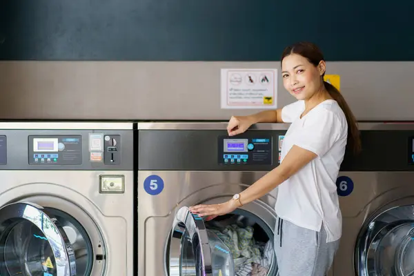Mutlu Asyalı güzel kadın self servis çamaşır makinesi kullanıyor KIOSK ya da otomatik çamaşır makinesi satıcısı. Bir kadın markette kendi kendine çalışan bir çamaşır makinesiyle etkileşime geçiyor..