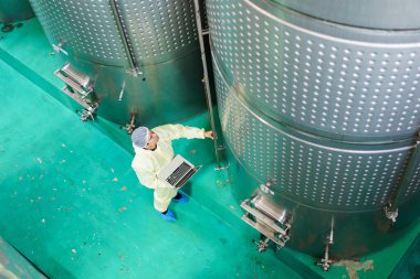 Kalite kontrol şefi yiyecek ve içecek imalat fabrikasının içini inceliyor. Kadın gıda bilimcisi içecek fabrikasındaki mayalanma tankını kontrol ediyor..