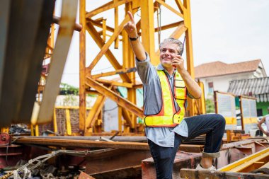 Senior foreman is performing the inspection at the construction site or factory, he's works with careless in dangerous place. A careless worker working at construction site without wearing helmet. clipart