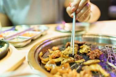 Mutlu Asyalı güzel kadın Kore restoranındaki ocakta ızgara yapıp geleneksel Kore barbeküsü yemekten hoşlanıyor. Asyalı kadın fırında domuz eti ve biftek pişiriyor..