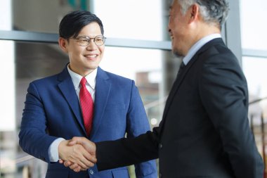 Asian businesspeople having a discussion together while walking inside the office building. Manager is talking with senior manager or chief of management. Businessmen in action portrait.