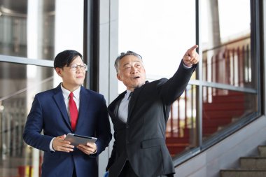 Asian businesspeople having a discussion together while walking inside the office building. Manager is talking with senior manager or chief of management. Businessmen in action portrait.