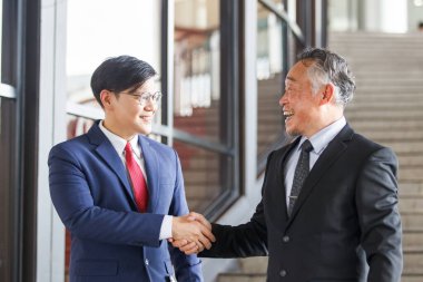 Asian businesspeople having a discussion together while walking inside the office building. Manager is talking with senior manager or chief of management. Businessmen in action portrait.