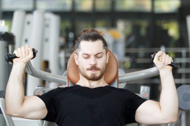 Good looking and muscular hispanic man doing a weight training exercise in the gym, a man focus a weight training at the arm and upper body. Healthy lifestyle concept.