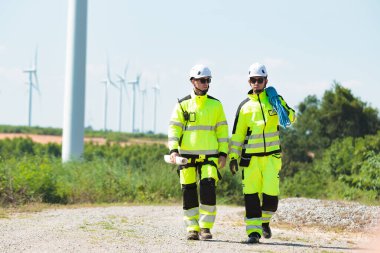 Team of professional electrical engineers in fully safety suit are working and discussing together at the windmill electric generating turbine. Electricians working at the site of windmill turbine.