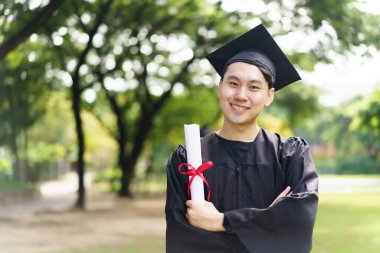 Male student in graduation gown has an excited and delighted expression as he receive his diploma upon graduating from university. An Asian student feel proud about academic achievement.