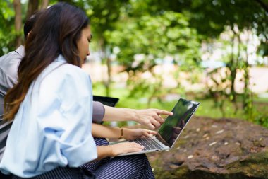 Diverse ethnicity university students are discussing together on laptop or notebook computer outside at park, people talking about the business on laptop computer outdoor. Modern working lifestyles.