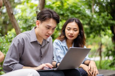 Diverse ethnicity university students are discussing together on laptop or notebook computer outside at park, people talking about the business on laptop computer outdoor. Modern working lifestyles.