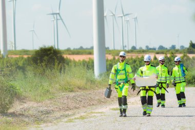 Team of professional electrical engineers in fully safety suit are working and discussing together at the windmill electric generating turbine. Electricians working at the site of windmill turbine.