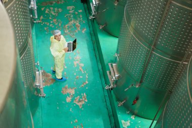 Kalite kontrol şefi yiyecek ve içecek imalat fabrikasının içini inceliyor. Erkek gıda bilim adamı içecek fabrikasındaki mayalanma tankını kontrol ediyor..