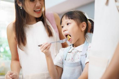 Neşeli Asyalı mutlu bir aile, anne ve kızı mutfakta birlikte kahvaltı etmekten ve yemek yapmaktan zevk alıyorlar. Hamile bir kadın, kocası ve kızıyla mutfakta kahvaltı hazırlar..