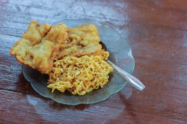 Kahvaltı tabağının fotoğrafı masanın üstünde 2 kızarmış tempeh 'li kızarmış erişte menüsü ve cam bir tabakta servis ediliyor.