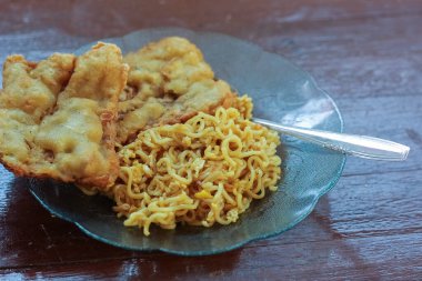 Kahvaltı tabağının fotoğrafı masanın üstünde 2 kızarmış tempeh 'li kızarmış erişte menüsü ve cam bir tabakta servis ediliyor.