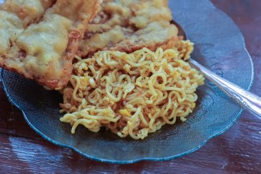 Kahvaltı tabağının fotoğrafı masanın üstünde 2 kızarmış tempeh 'li kızarmış erişte menüsü ve cam bir tabakta servis ediliyor.