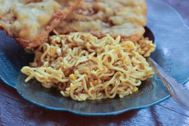 Kahvaltı tabağının fotoğrafı masanın üstünde 2 kızarmış tempeh 'li kızarmış erişte menüsü ve cam bir tabakta servis ediliyor.