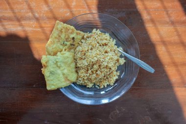 Kahvaltı tabağının fotoğrafı masanın üstünde. Yanında da yumurta pilavı ve 2 kızarmış tempeh ve cam bir tabakta servis ediliyor.