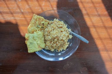 Kahvaltı tabağının fotoğrafı masanın üstünde. Yanında da yumurta pilavı ve 2 kızarmış tempeh ve cam bir tabakta servis ediliyor.