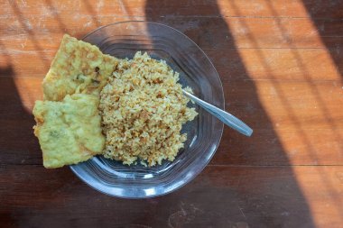 Kahvaltı tabağının fotoğrafı masanın üstünde. Yanında da yumurta pilavı ve 2 kızarmış tempeh ve cam bir tabakta servis ediliyor.