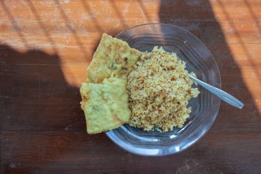 Kahvaltı tabağının fotoğrafı masanın üstünde. Yanında da yumurta pilavı ve 2 kızarmış tempeh ve cam bir tabakta servis ediliyor.