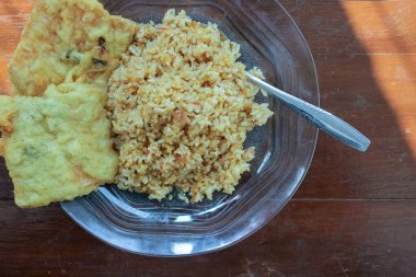 Kahvaltı tabağının fotoğrafı masanın üstünde. Yanında da yumurta pilavı ve 2 kızarmış tempeh ve cam bir tabakta servis ediliyor.