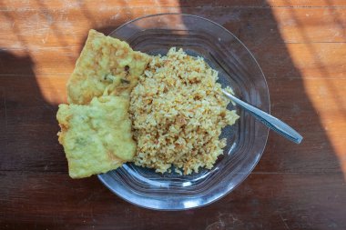 Kahvaltı tabağının fotoğrafı masanın üstünde. Yanında da yumurta pilavı ve 2 kızarmış tempeh ve cam bir tabakta servis ediliyor.
