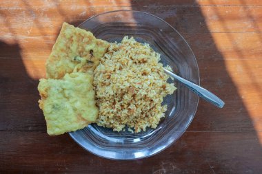 Kahvaltı tabağının fotoğrafı masanın üstünde. Yanında da yumurta pilavı ve 2 kızarmış tempeh ve cam bir tabakta servis ediliyor.