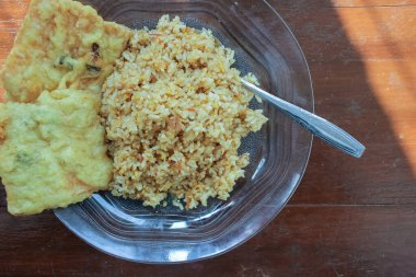 Kahvaltı tabağının fotoğrafı masanın üstünde. Yanında da yumurta pilavı ve 2 kızarmış tempeh ve cam bir tabakta servis ediliyor.