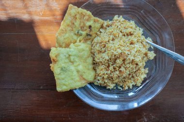 Kahvaltı tabağının fotoğrafı masanın üstünde. Yanında da yumurta pilavı ve 2 kızarmış tempeh ve cam bir tabakta servis ediliyor.